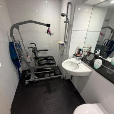 Hoist and shower chair stored in shower area when not in use.